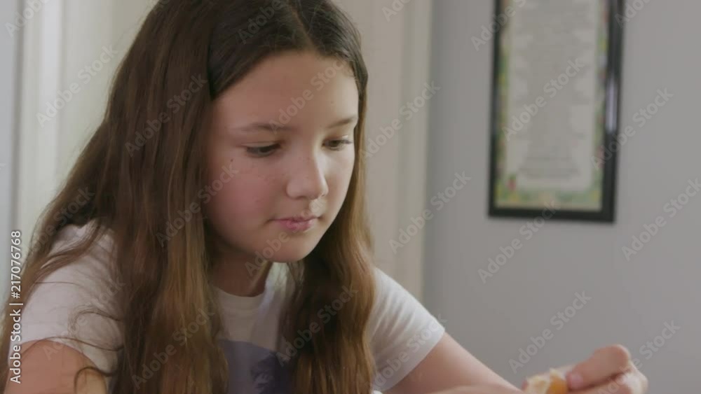Cute little brown haired girl eats an orange at the dining room table. Cute little brown haired girl eats an orange at the dining room table.