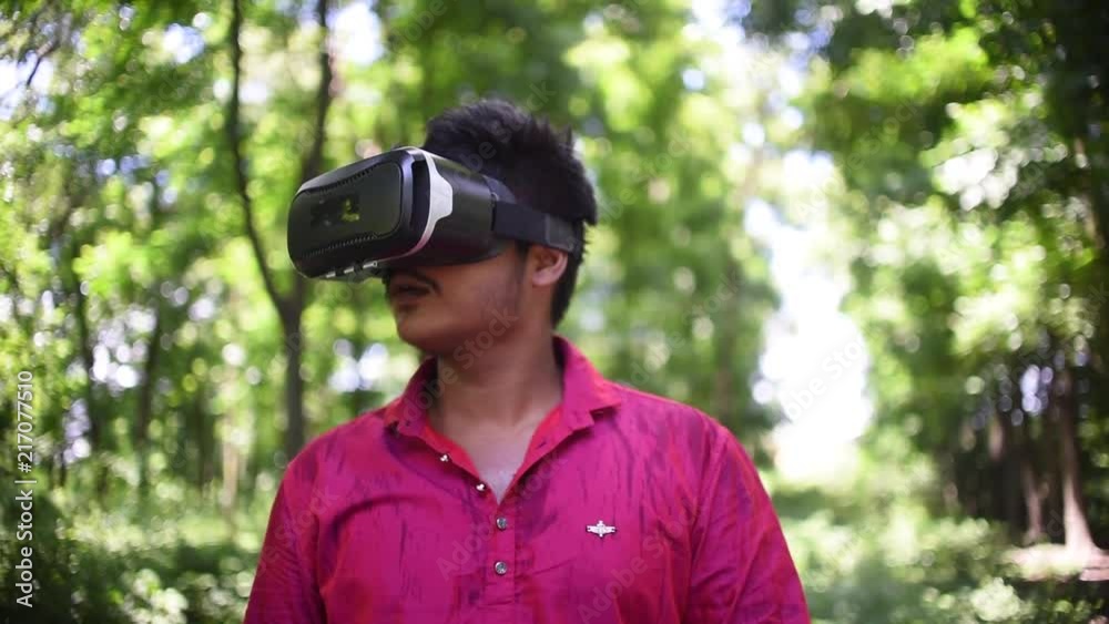 A South Asian Indian boy watching and enjoying VR headset Virtual reality in a forest and shooting with his fingers A South Asian Indian boy watching and enjoying VR headset Virtual reality in a forest and shooting with his fingers