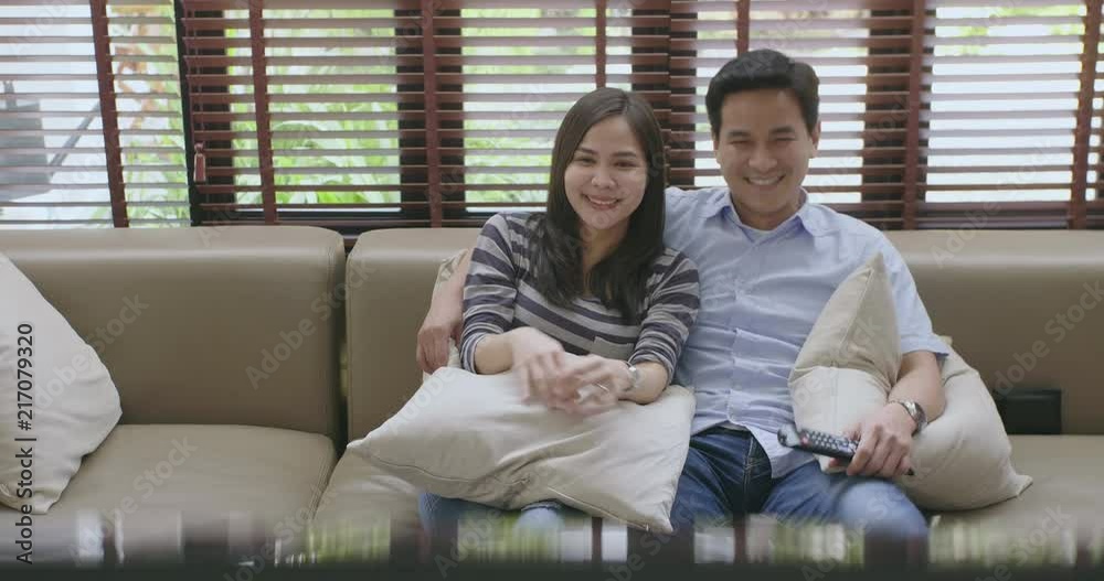Young asian sweet couple watch television embraced on the sofa in the new house and watch a movie together. Concept of: leisure, relax, tv. Young asian sweet couple watch television embraced on the sofa in the new house and watch a movie together. Concept of: leisure, relax, tv.