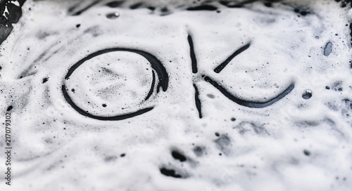The word "Ok" is written on a soapy foam. Detergent for pan, dishes or car.