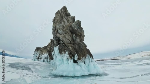 Travel of woman on ice of Lake Baikal. POV view. Trip to winter island. Girl is walking at foot of ice rocks. Traveler looks at beautiful ice grotto. Hiker wears sports glasses, silver jacket photo