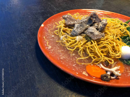 crispy noodles topped with  meat and vegetable  in orange dish on black table, delicious of Thai street food , Name of this menu in Thailand : 