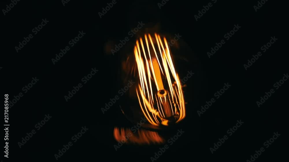 One orange glow Edison bulb glowing on in the dark, and then turning off.