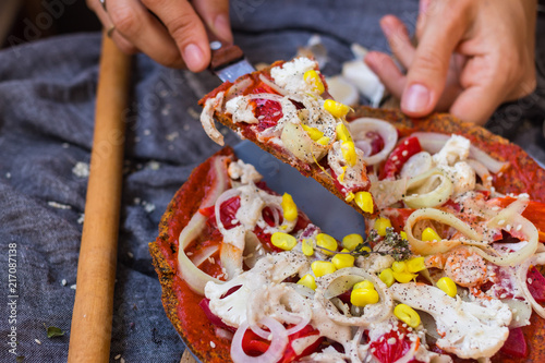 Woman hands hold a piece of raw vegan pizza with dehydrated dough, raw tomato sauce, vegan mayonnaise, corn and fresh vegetables. Healthy Italian food © Viktor Kochetkov