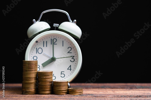 Alarm clock and coins stacks on working table in dark room, time for savings money concept, banking and business concept.