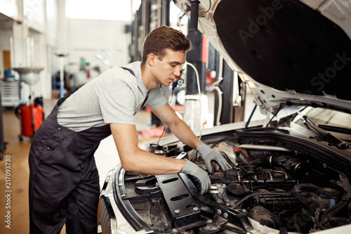 A qualified automechanic is searching for bugs at a car repair service