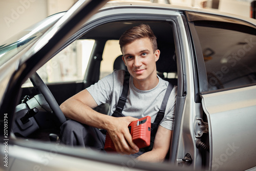 An attractive young man is sitting in a car being repaired by him