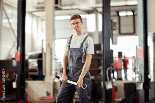 A young car mechanic is standing with a monkey wrench in his hands