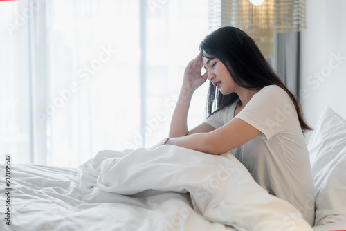 Attractive young Asian woman wake up on her bed looking unhappy and feeling sick..