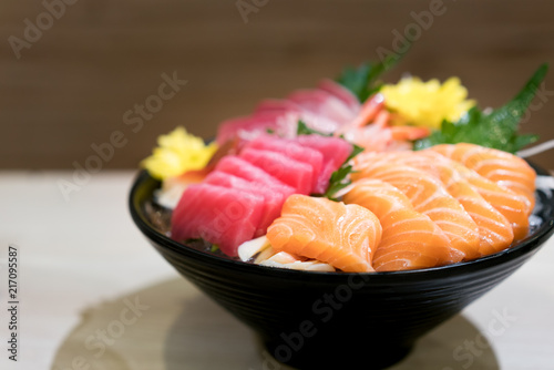 Mixed sliced fish sashimi on ice in black bowl. Sashimi Salmon Tuna Hamachi Prawn and Surf Calm set, raw fish, japanese food in Asian restuarant.