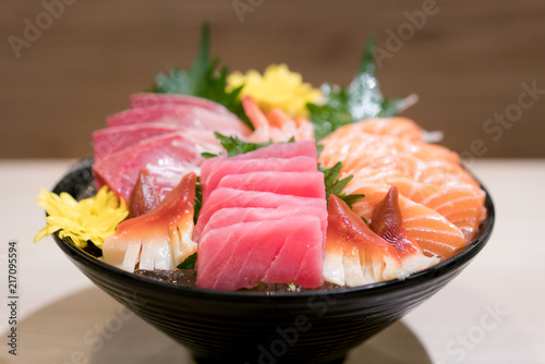 Mixed sliced fish sashimi on ice in black bowl. Sashimi Salmon Tuna Hamachi Prawn and Surf Calm set, raw fish, japanese food in Asian restaurant.