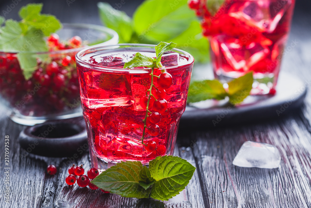 Red currant cocktail with ice and fresh mint on a black wooden table