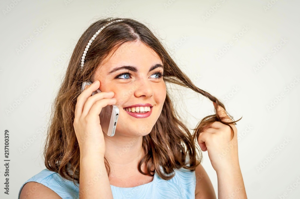 A happy smiling beautiful Caucasian girl with deep blue eyes talking on a phone and flirting with her boyfriend, touching her hair. A happy smiling beautiful Caucasian girl with deep blue eyes talking on a phone and flirting with her boyfriend, touching her hair.