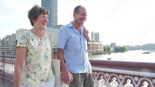 Slow motion steady cam view of active senior caucasian tourist couple walking in on blackfriars bridge london with the river thames behind themes of sightseeing active seniors direction on the move