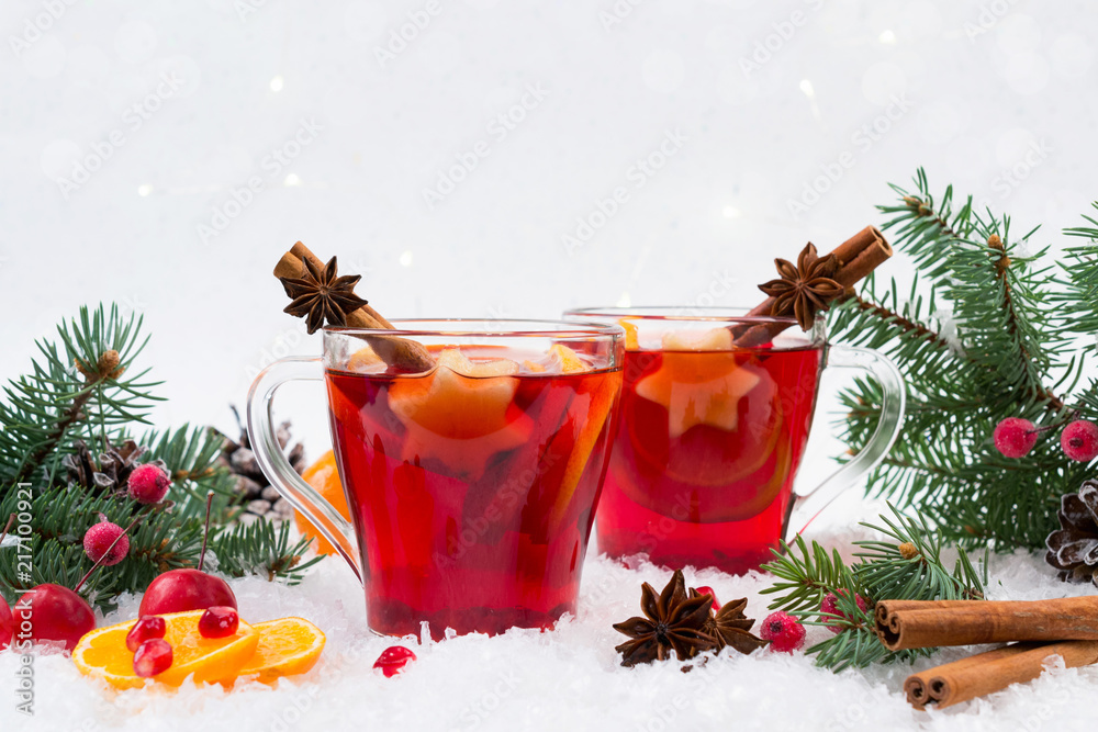 Hot mulled spiced red wine in glass mug with with festive decoration lights and gingerbread . On white snow background Hot mulled spiced red wine in glass mug with with festive decoration lights and gingerbread . On white snow background