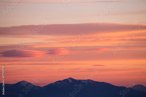 A view of some mountains top, beneath a beautiful, warm colored sky at sunset
