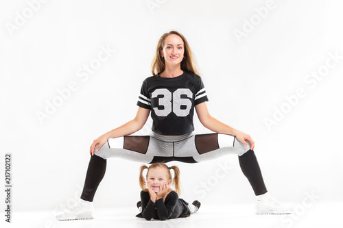 Portrait of healthy family of mother sitting in fitness pose above little daughter hisolated at white background. photo