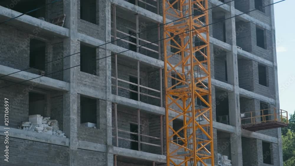 Multi-storey under construction building and construction crane on the background of clear sky. Close-up. Multi-storey under construction building and construction crane on the background of clear sky. Close-up.