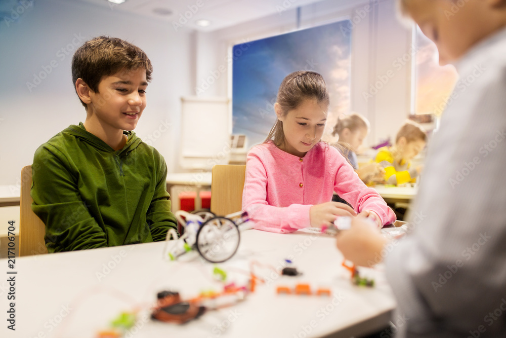 education, children, technology, science and people concept - group of happy kids building robots at robotics school lesson