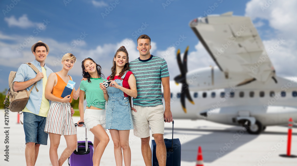 Obraz premium summer holidays, tourism and vacation concept - group of happy friends with travel bags, air tickets and camera over airplane background