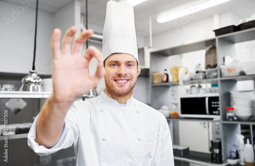 cooking, profession and people concept - happy male chef cook in toque at restaurant kitchen showing ok hand sign