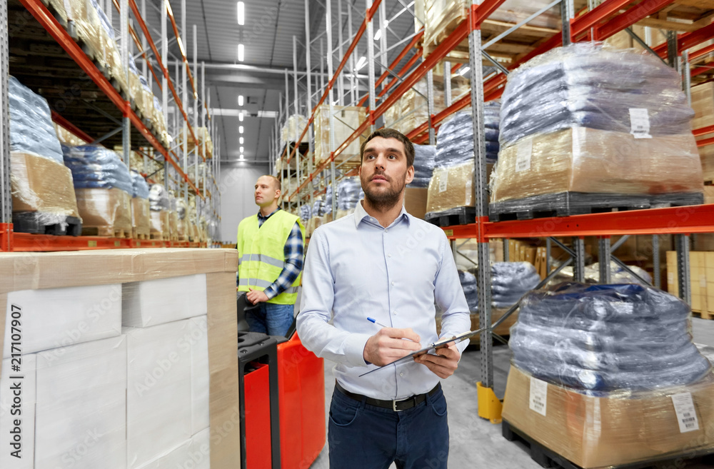 logistic business, shipment and people concept - businessman with clipboard and worker loading goods by forklift at warehouse logistic business, shipment and people concept - businessman with clipboard and worker loading goods by forklift at warehouse