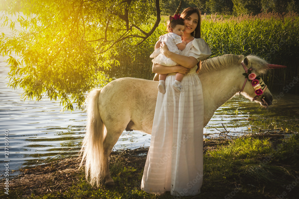 beautiful young mother with a little daughter in the woods at a photo shoot near a pond with a unicorn