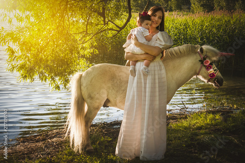 Obraz na płótnie beautiful young mother with a little daughter in the woods at a photo shoot near a pond with a unicorn w salonie