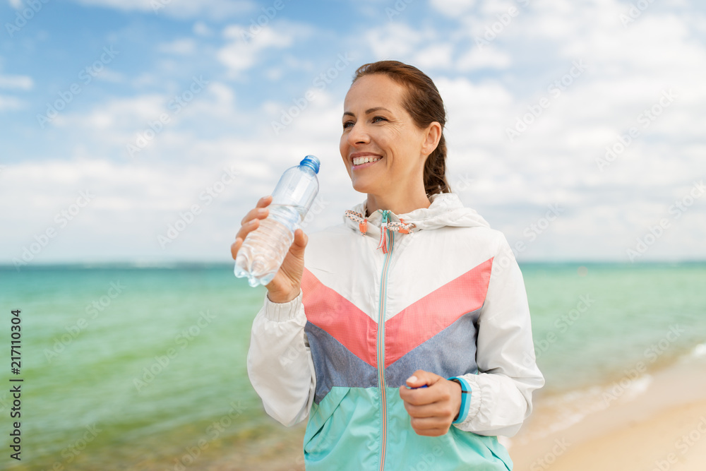 fitness, sport and healthy lifestyle concept - woman drinking water after exercising on beach fitness, sport and healthy lifestyle concept - woman drinking water after exercising on beach
