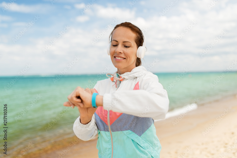 sport, technology and healthy lifestyle concept - smiling woman with headphones and fitness tracker exercising on beach sport, technology and healthy lifestyle concept - smiling woman with headphones and fitness tracker exercising on beach