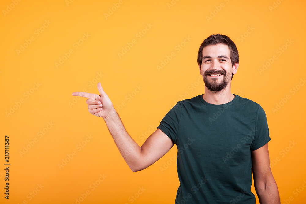 Cheerful smiling man pointing at his right at copyspace available for your advertisement or promotion. Isolated on orange backgorund in studio. Cheerful smiling man pointing at his right at copyspace available for your advertisement or promotion. Isolated on orange backgorund in studio.