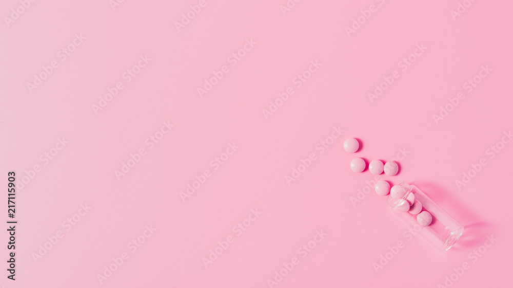 top view of pink medicines spilled from bottle on pink surface