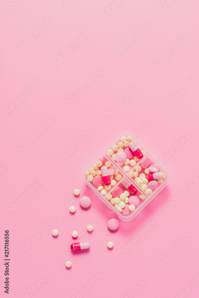 top view of plastic container with various pills on pink