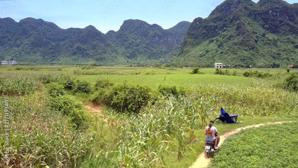 couple on motorbike passes by local man on road side