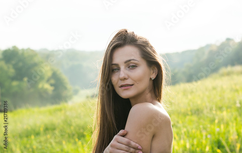 Portrait of a beautiful young woman with bare shoulders in the sunlight on a meadow with wildflowers at the rural background