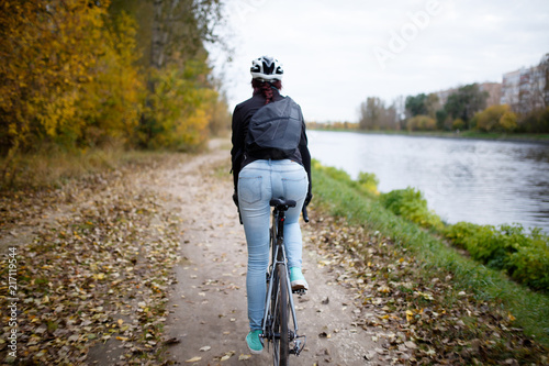 Photo from back of girl in helmet riding bicycle on river bank