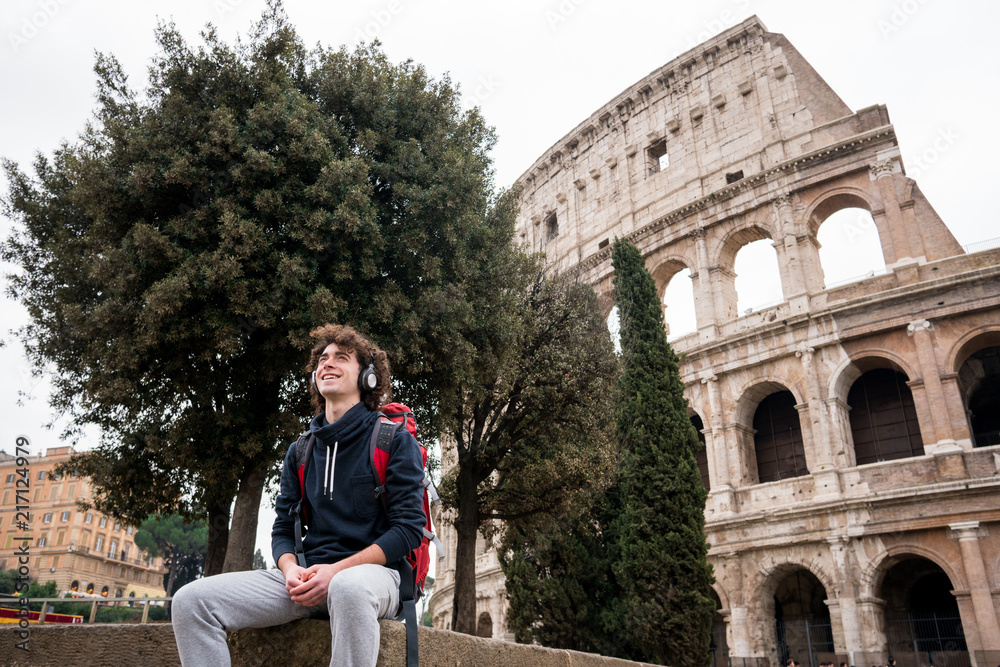 Handsome young man with headphones listening to music in front of Colosseum in Rome