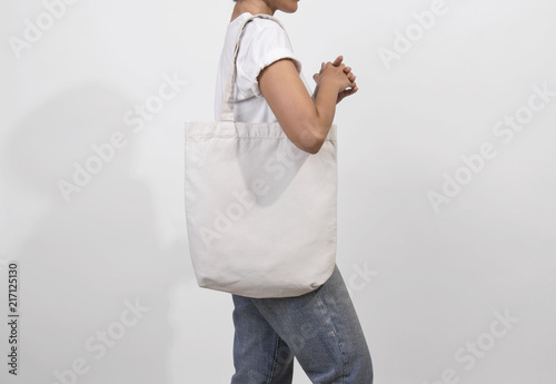 Dziewczyna trzyma torby płótno tkaniny dla makieta pusty szablon na białym tle na szarym tle.