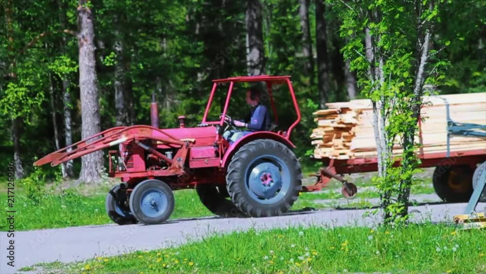 Farmer on Tractor Pulling Cut Lumber Through the Countryside in Sweden Farmer on Tractor Pulling Cut Lumber Through the Countryside in Sweden