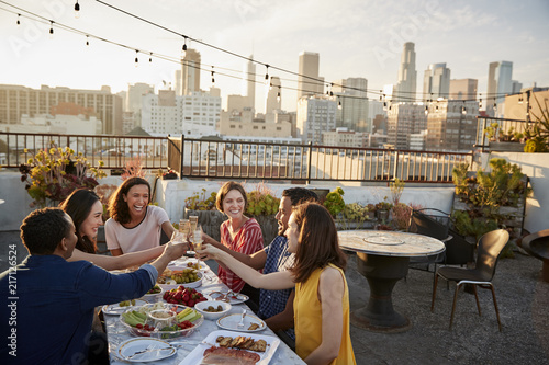 Photography Friends Gathered On Rooftop Terrace For Meal With City Skyline In Background