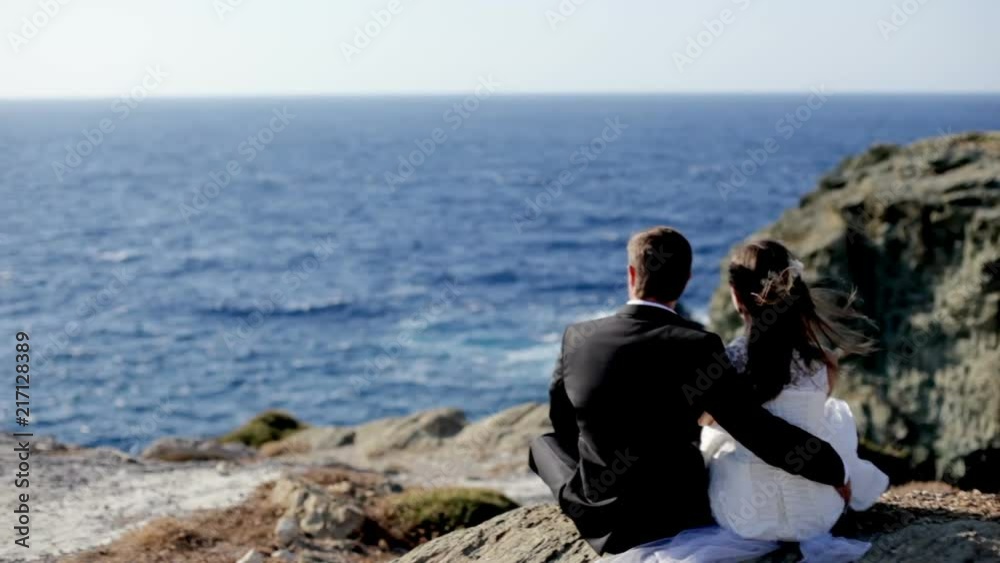 Happy bride and groom tenderly embrace on the stone shore of the sea on a sunny day. Greece Happy bride and groom tenderly embrace on the stone shore of the sea on a sunny day. Greece