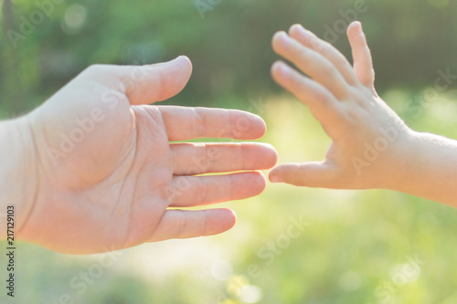 The hand of an adult and a child stretches towards each other.