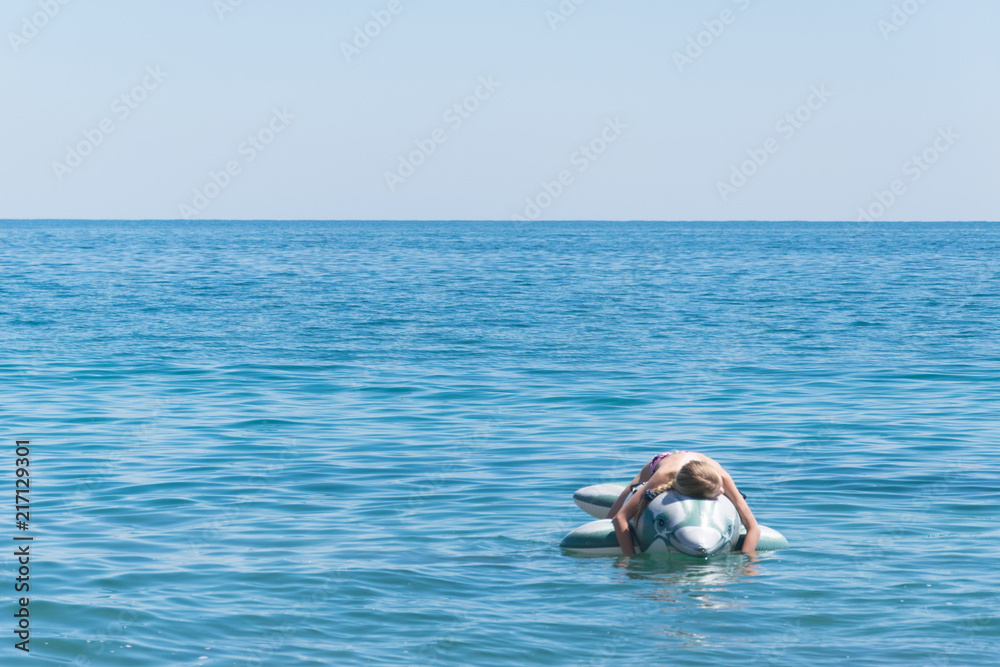 The girl is swimming on an inflatable toy-dolphin on the sea of the ocean. Rest on the water, vacation.