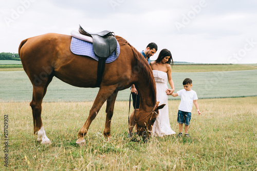 parents and son standing near beautiful brown horse on field