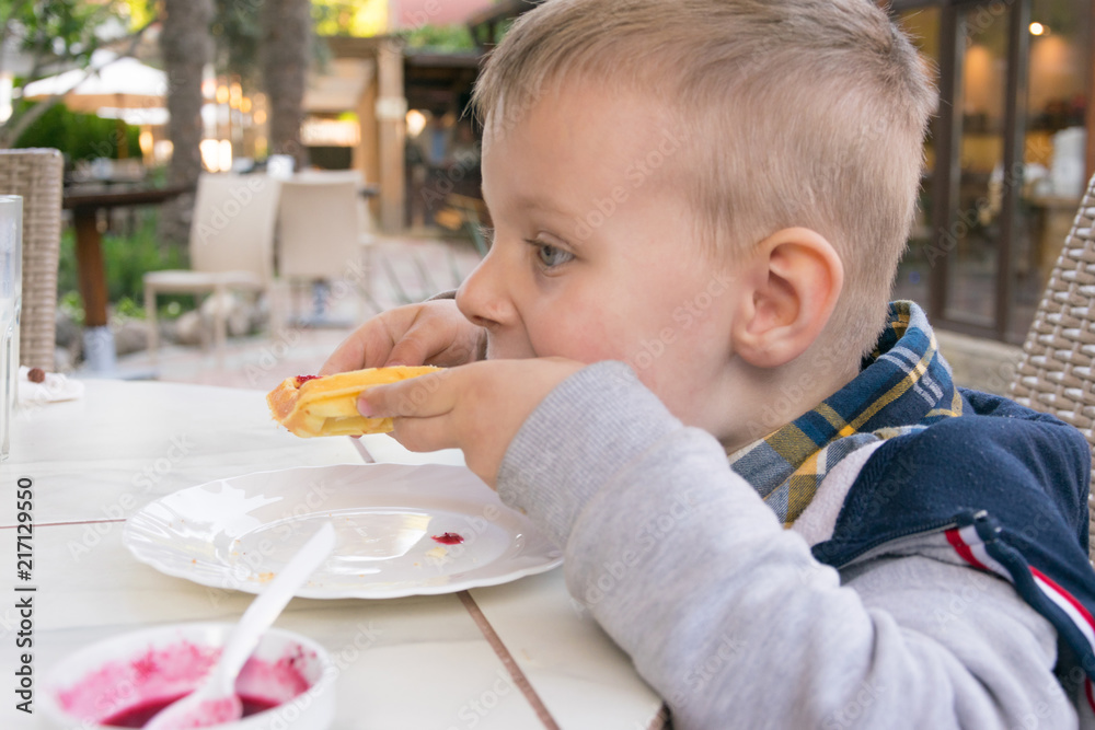 A little boy eats dessert (Belgian waffles with jam) in a cafe. A little boy eats dessert (Belgian waffles with jam) in a cafe.
