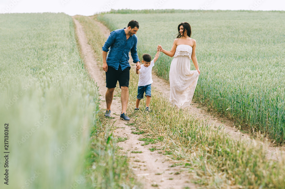 parents and son holding hands and walking on path in green field parents and son holding hands and walking on path in green field