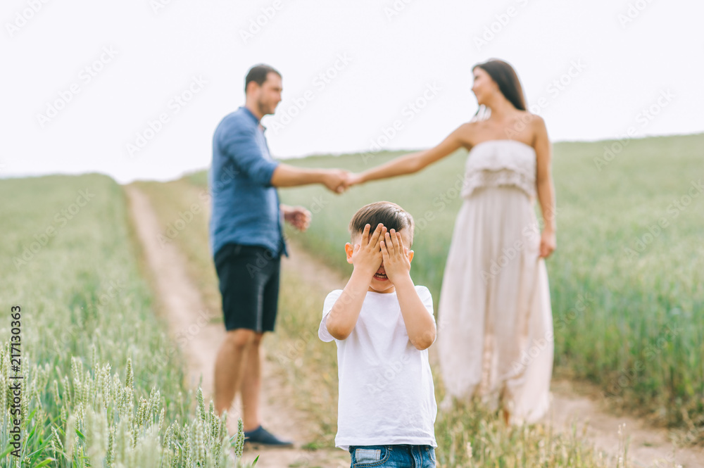 parents holding hands and son covering eyes on path in field parents holding hands and son covering eyes on path in field