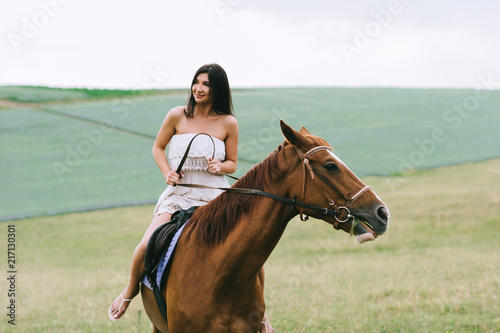beautiful woman riding brown horse on green field