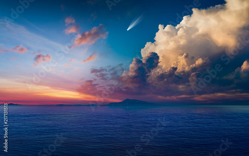 Bright comet in glowing sunset sky above dark blue sea