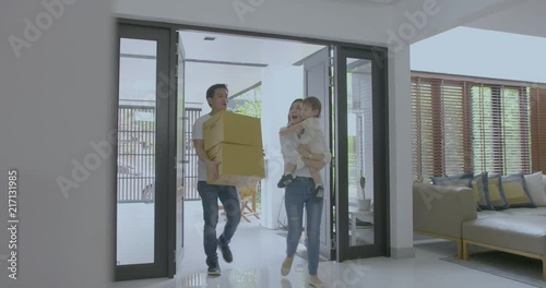 Happy family with kids holding boxes entering new modern house, family relocating concept.